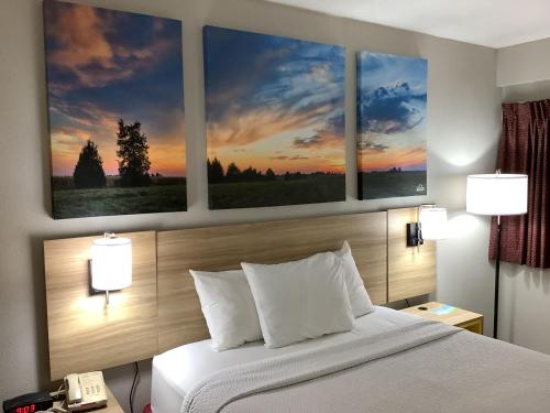 a bedroom with a bed with four paintings on the wall at Days Inn by Wyndham Kingdom City in Kingdom City