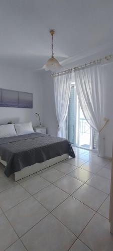 a white bedroom with a bed and a large window at White Beach Appartment in Yerakiní
