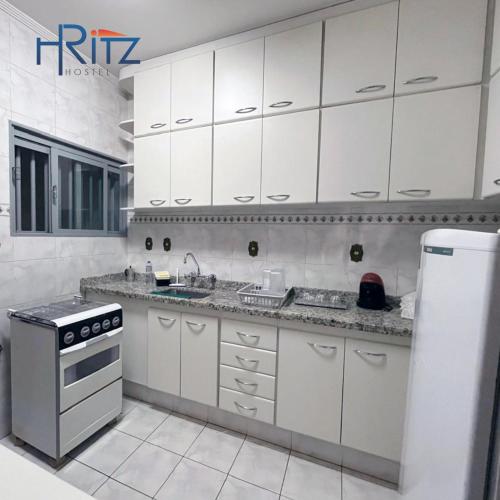 a kitchen with white cabinets and a sink and a refrigerator at Ritz Hostel in Araçatuba