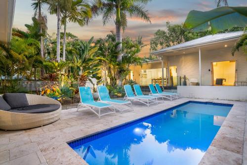 a swimming pool with blue chairs and a house at Cove Studios in Byron Bay
