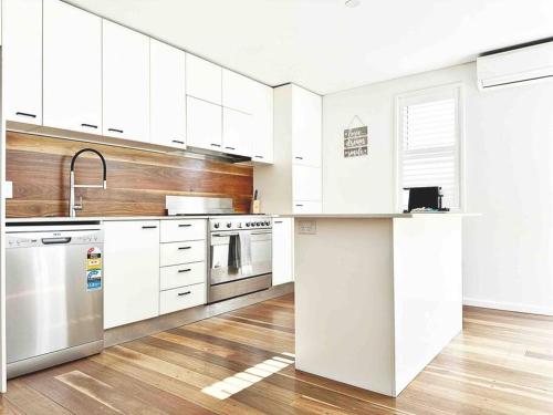 a kitchen with white cabinets and stainless steel appliances at Palm Rest - 2BR Beachside Escape On Towradgi Beach in Towradgi