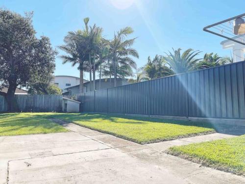 a fence in front of a yard with palm trees at Palm Rest - 2BR Beachside Escape On Towradgi Beach in Towradgi