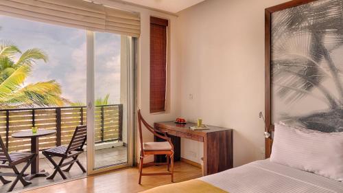 a bedroom with a bed and a desk and a balcony at Jetwing Sea in Negombo