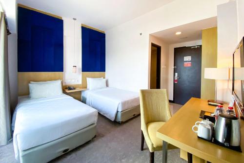 a hotel room with two beds and a desk and a table at Swiss-Belinn Malang in Malang