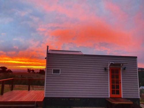 a small house with a red door and a sunset at Gem View - Tiny home in Barwite