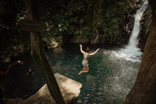 a woman jumping into a waterfall in the water at Maha Hills Resort by Mahaprana Experience in Lovina