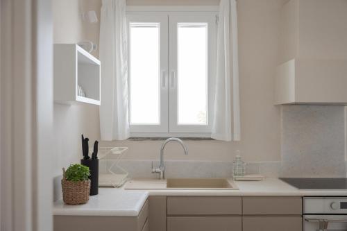a white kitchen with a sink and a window at Morfes Luxury Apartments in Triandáros