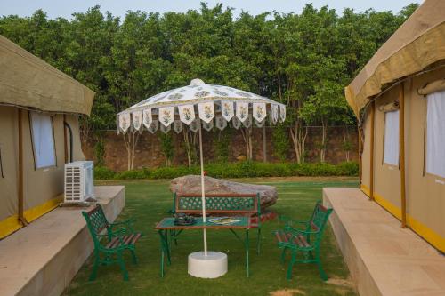 a table and chairs under an umbrella in a yard at Elivaas 5 BHK with Pool, Tents & Pond - Kaimalgarh Farmstay in Bhundsi