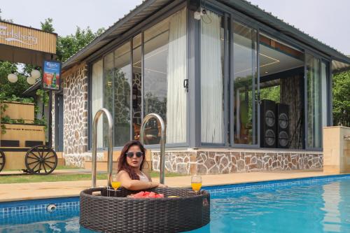 a woman sitting in a pool with a drink at Elivaas 5 BHK with Pool, Tents & Pond - Kaimalgarh Farmstay in Bhundsi