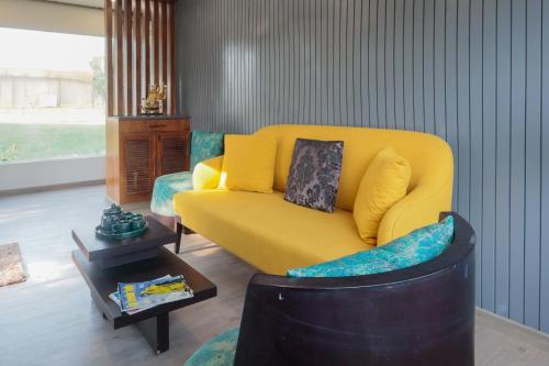 a living room with a yellow couch and a table at Elivaas 5 BHK with Pool, Tents & Pond - Kaimalgarh Farmstay in Bhundsi