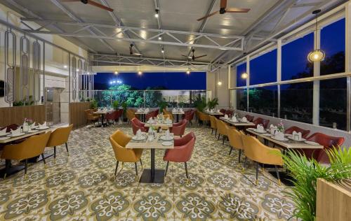 a restaurant with tables and chairs and large windows at Grand Continent Mysore A Sarovar Portico Affiliate Hotel in Mysore