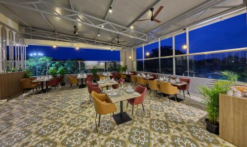 a restaurant with tables and chairs and large windows at Grand Continent Mysore A Sarovar Portico Affiliate Hotel in Mysore