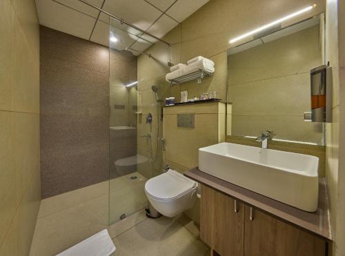 a bathroom with a sink and a toilet and a mirror at Grand Continent Mysore A Sarovar Portico Affiliate Hotel in Mysore