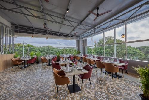a restaurant with tables and chairs and large windows at Grand Continent Mysore A Sarovar Portico Affiliate Hotel in Mysore