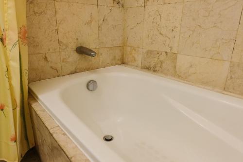 a white bath tub in a bathroom with a tile wall at Best Location 2BR at Braga City Walk Apartment By Travelio in Bandung