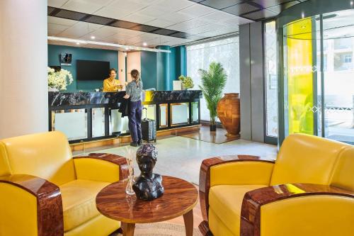 a lobby with yellow chairs and a man standing at a counter at Hôtel Charlemagne by Happyculture in Lyon