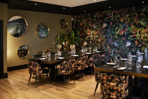 a dining room with tables and chairs and a floral wall at The Originals Boutique, La Maison Rouge, Lens Ouest in Noeux-les-Mines