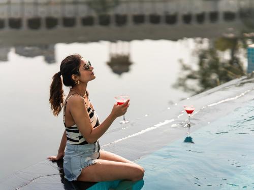 a woman sitting next to a swimming pool holding a glass of wine at Moustache Udaipur Verandah in Udaipur