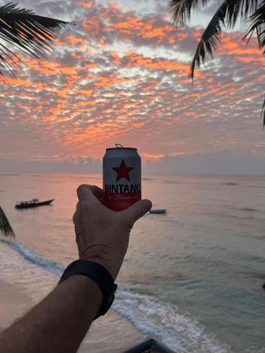 a hand holding a cup of drinking on the beach at Sunset Surfing Villas Mentawai in Tuapejat