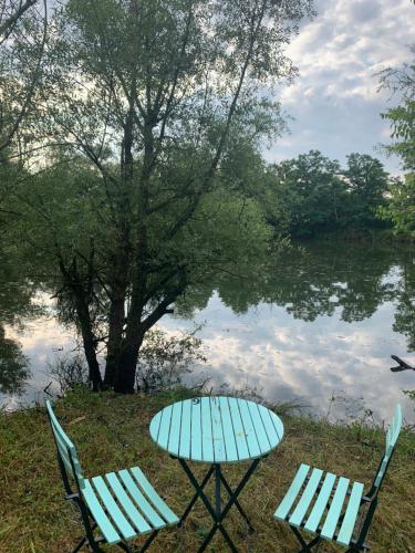 2 chaises et une table à côté d'un lac dans l'établissement Nuit en van au bord étang privé, à Saint-Sauveur