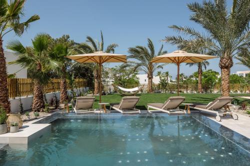 a pool with chairs and umbrellas and palm trees at 7Pines Resort Ibiza, part of Destination by Hyatt in San Jose