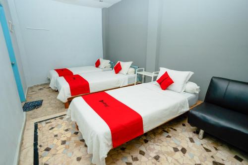 two beds in a room with a chair and a couch at RedDoorz near RSUD Kota Mataram in Mataram