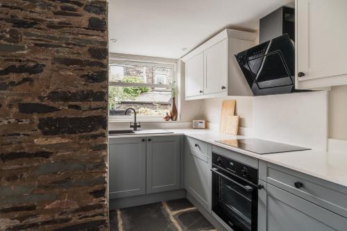 a kitchen with white cabinets and a stone wall at Brantwood - 4 bed home Ambleside in Ambleside