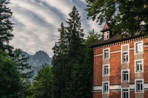 a red brick building with a tower in front of trees at Rewita Kościelisko-Zakopane in Kościelisko