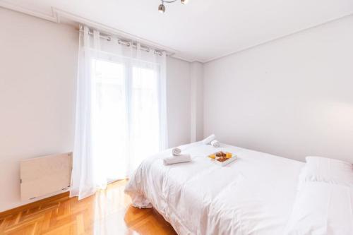 a white bedroom with a white bed and a window at Charming Coastal Apartment Steps from the Beach in San Juan de la Arena