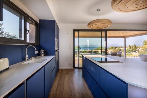 une cuisine avec des placards bleus et une grande fenêtre dans l'établissement Villa de la Madrague Vue Mer à 200m de la Plage sur La Presqu' île de Giens Sea and Mountain Pleasure, à Hyères