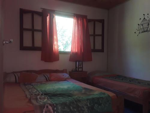 a bedroom with two beds and a window with red curtains at Cabañas La Fiaca in Los Manantiales