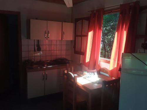 une cuisine avec des rideaux rouges, une table et une fenêtre dans l'établissement Cabañas La Fiaca, à Los Manantiales