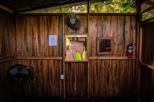 a wooden wall with a window and a fan at Flutterby House Hostel in Uvita