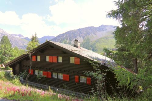 a wooden house with red windows and mountains in the background at Chalet Traumhaus in Arosa