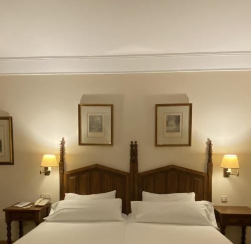 two beds in a bedroom with two lamps on the wall at Parador de Vilalba in Villalba