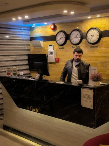 a man sitting at a counter with clocks on the wall at Petra Corner Hotel in Petra