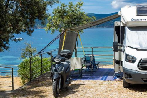 a motor scooter parked next to a truck at Camping Village Le Calanchiole in Capoliveri