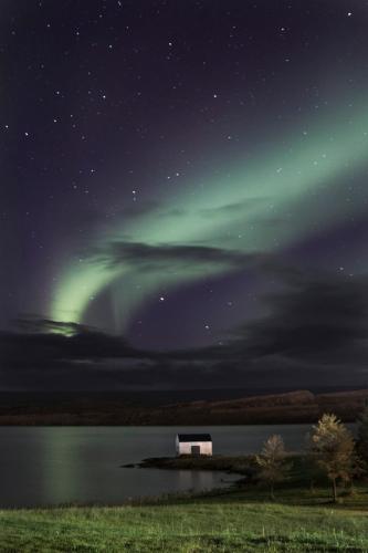a barn under the northern lights in the sky over a lake at Gistihúsið - Lake Hotel Egilsstadir in Egilsstadir