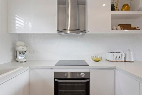 a kitchen with white cabinets and a stove top oven at Stylish Zen Bungalow w Firepit + Walk to Beach in Smiths Beach