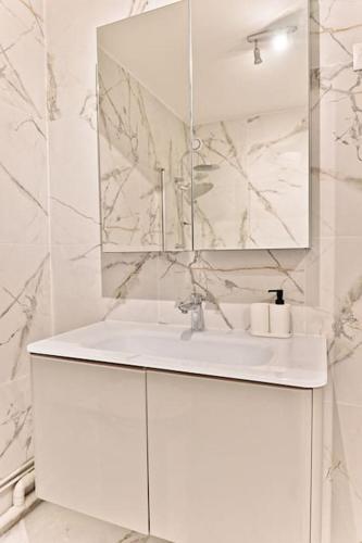une salle de bain blanche avec un lavabo et un miroir dans l'établissement Appartement spacieux et paisible Paris 19ème, à Paris