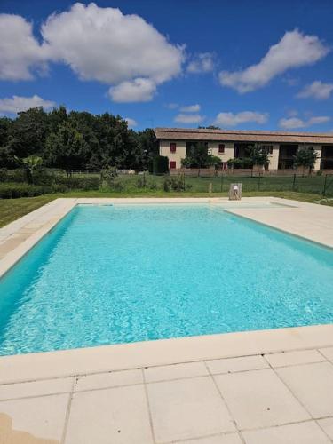 une grande piscine bleue avec une maison en arrière-plan dans l'établissement Gite du Chêne Pardaillan, à Pardaillan