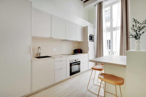 une cuisine avec des placards blancs, une table et des tabourets dans l'établissement Charming Apartment - 1BR-5P - Sentier, à Paris