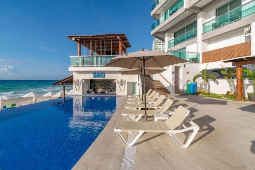 a pool with chairs and an umbrella and the ocean at Beachfront Apartment by Andiani Travel in Cancún
