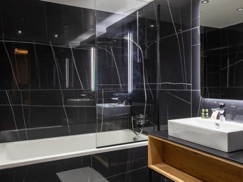 La salle de bains est pourvue de carrelage noir, d'un lavabo et d'une baignoire. dans l'établissement Appartement élégant 10 personnes avec terrasse et vue sur vallée - FR-1-275-216, à La Rosière