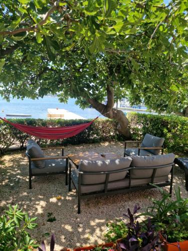 a hammock and two chairs under a tree at Apartmani Rukavina in Rab