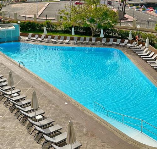 a large swimming pool with lounge chairs and umbrellas at Apartamentos Portonovo in Puerto Rico de Gran Canaria