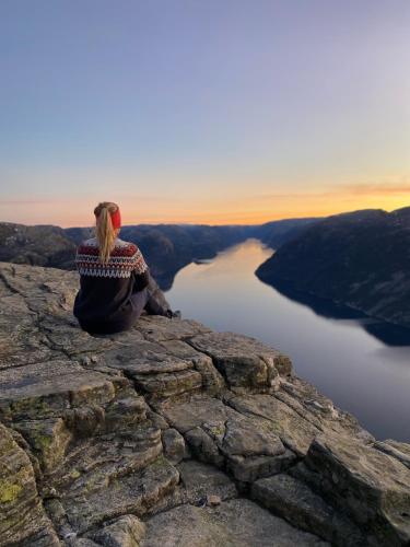 a woman sitting on the edge of a cliff overlooking a lake at Beautiful Beach line Cabin with sauna near Pulpit Rock in Forsand