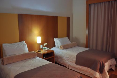 um quarto de hotel com duas camas e uma mesa com um candeeiro em Cegil Hotel Boulevard em Resende