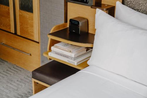 a bed with a nightstand with books and a alarm clock at The Jewel Hotel, New York in New York
