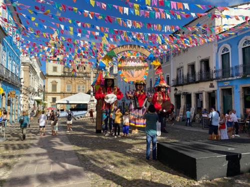 a group of people standing in a street with flags and performers at A Casa dos Mestres in Salvador